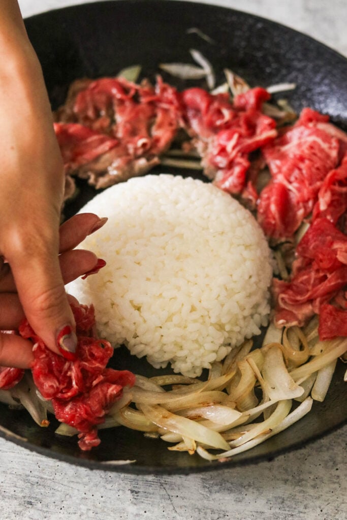 placing meat on top of grilled onions with rice in the middle 