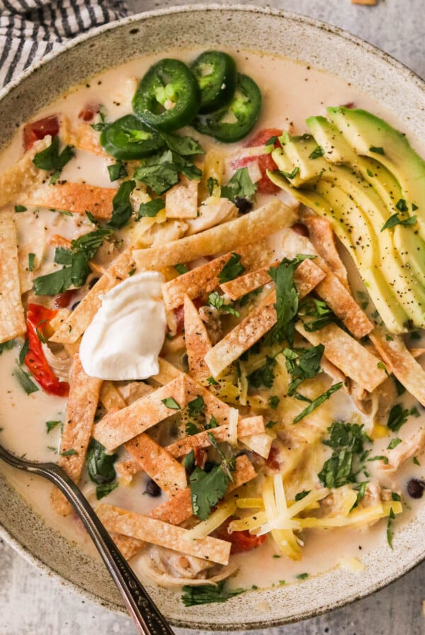 creamy slow cooke chicken tortilla soup in a bowl topped with avocado, sour cream, and tortilla strips
