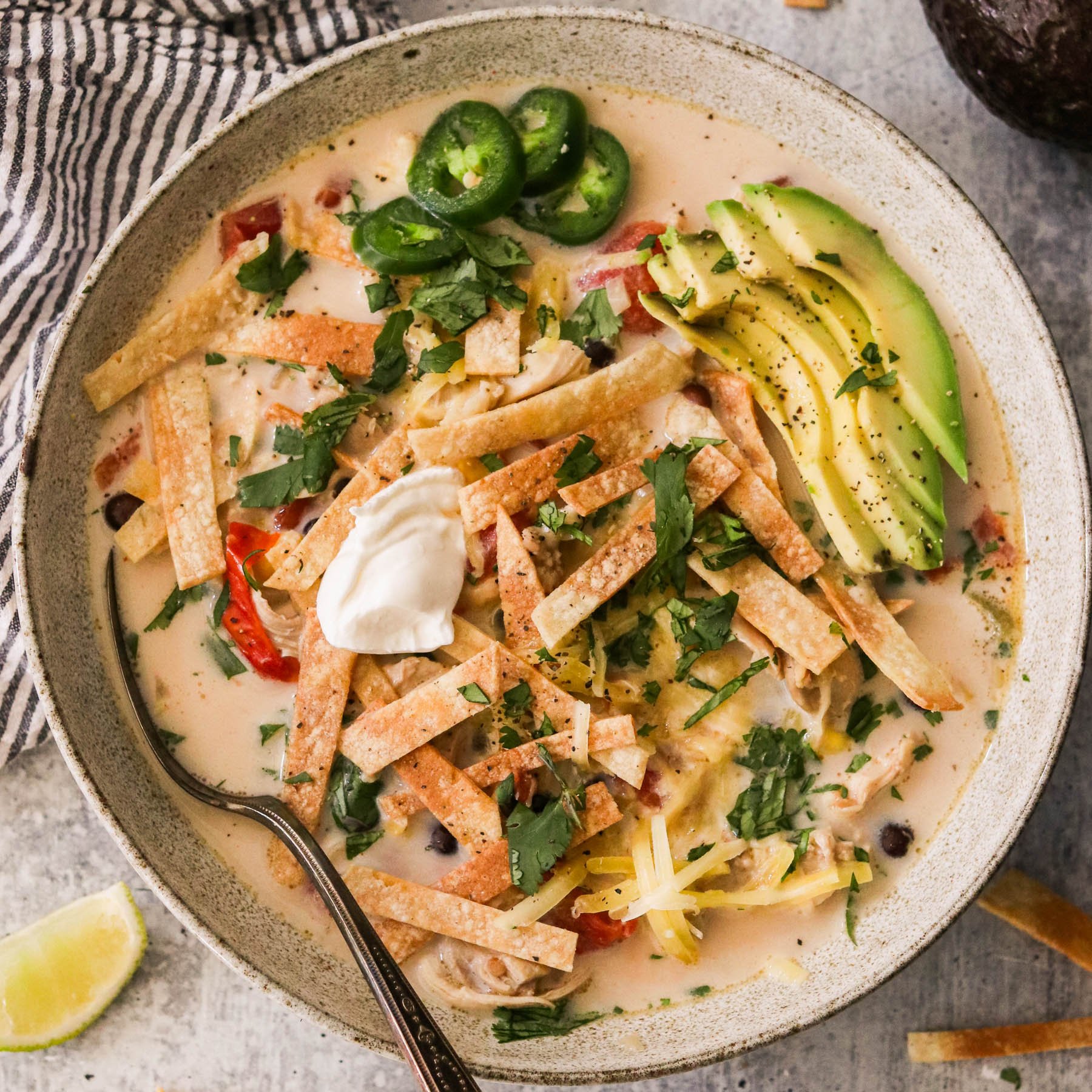 Creamy slow cooker chicken tortilla soup in a bowl topped with avocado, sour cream, and tortilla strips.