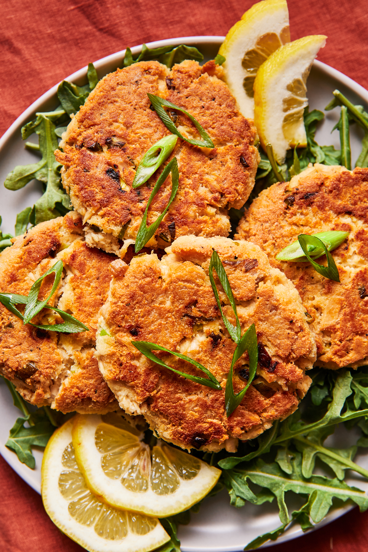 Stack of tuna patties on a ceramic plate with herbs and lemon slices