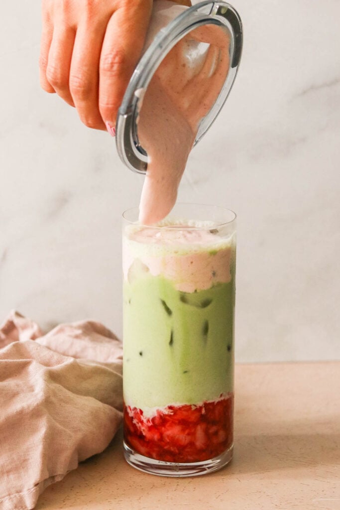 pouring strawberry cold foam on top of the matcha. 