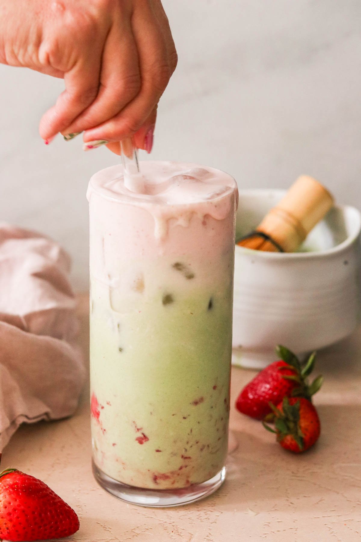 a hand stirring a glass straw inside of a strawberry matcha latte. 