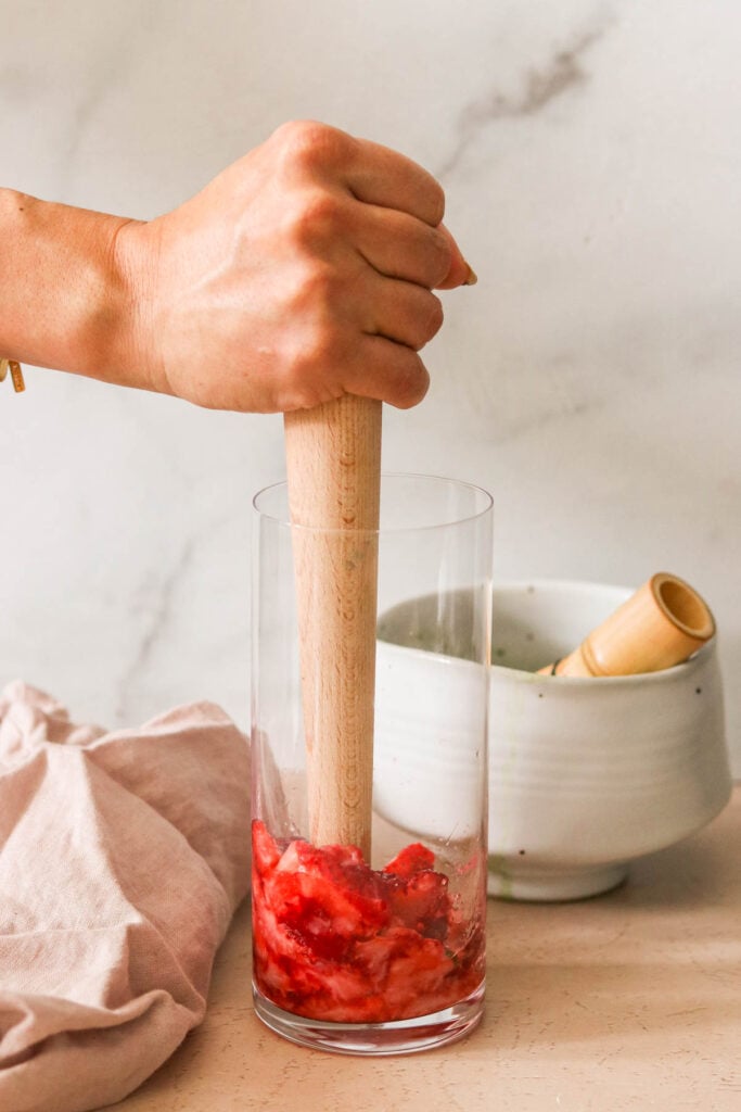 a glass of fresh strawberries muddled with a wooden muddler