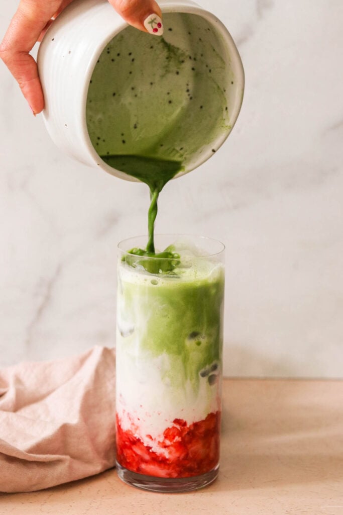 pouring matcha on top of strawberries and milk in a glass. 