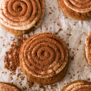 Soft tiramisu cookies topped with piped mascarpone frosting and dusted with cocoa powder on a white plate.