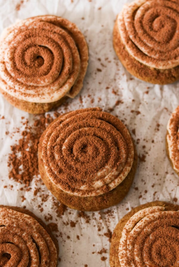 Soft tiramisu cookies topped with piped mascarpone frosting and dusted with cocoa powder on a white plate.