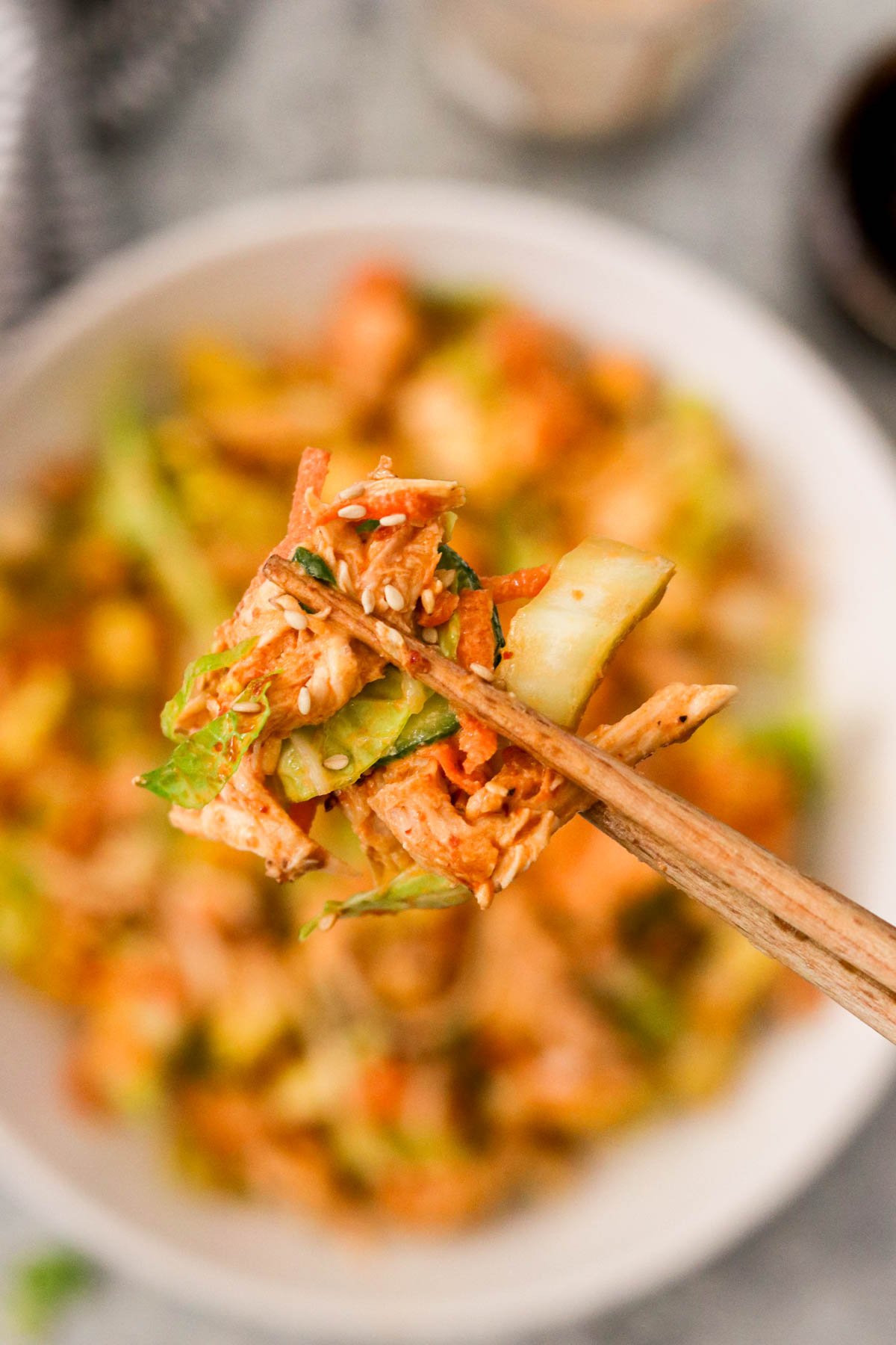Side angle shot of a forkful of bang bang chicken salad held with chopsticks
