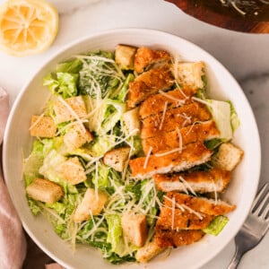 Overhead view of crispy chicken Caesar salad with romaine, golden croutons, and sliced air-fried chicken on a white plate