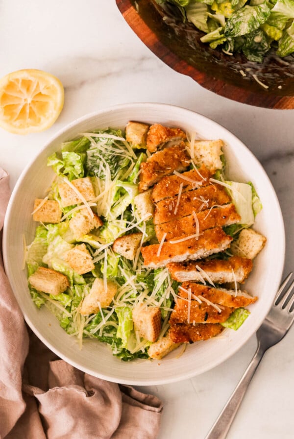 Overhead view of crispy chicken Caesar salad with romaine, golden croutons, and sliced air-fried chicken on a white plate