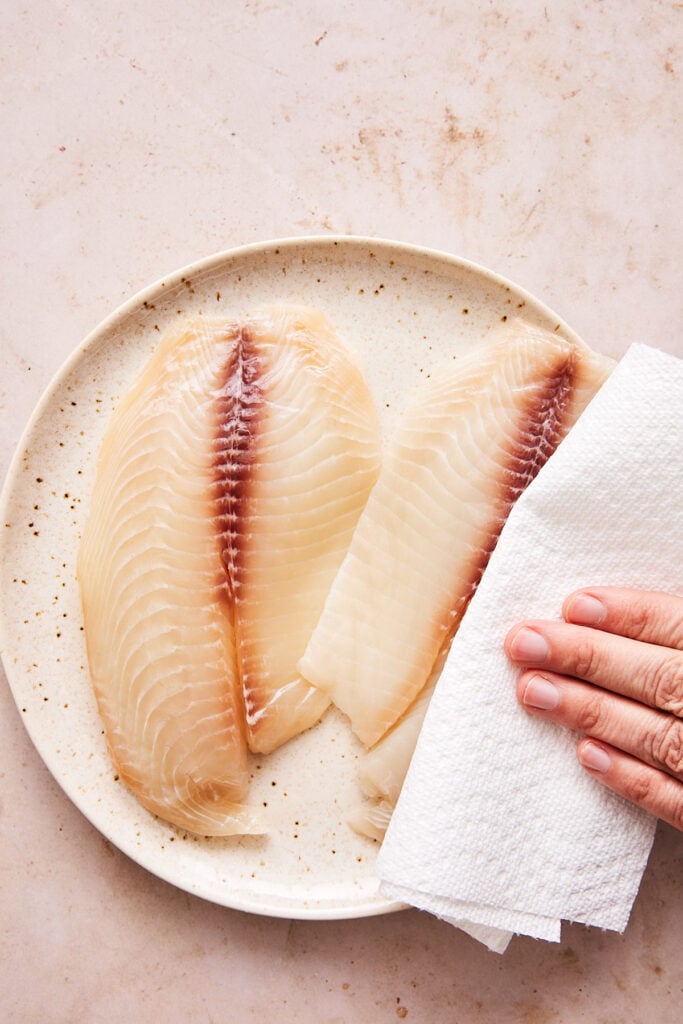 patting fresh tilapia with a paper towel