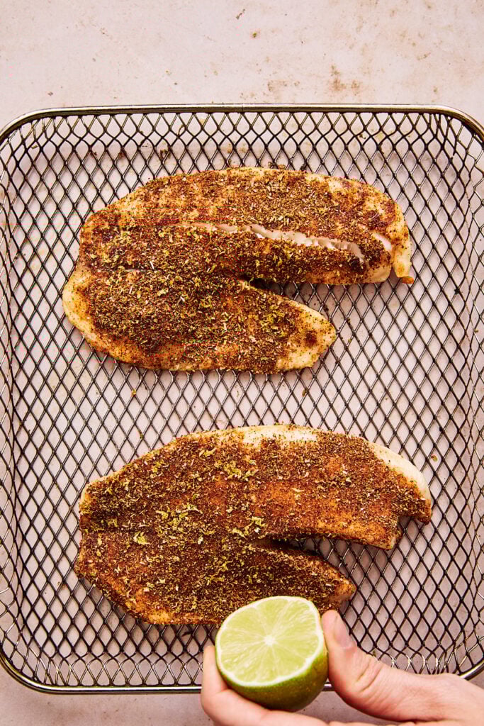 tilapia rubbed with a spice mixture and a hand squeezing lime on top