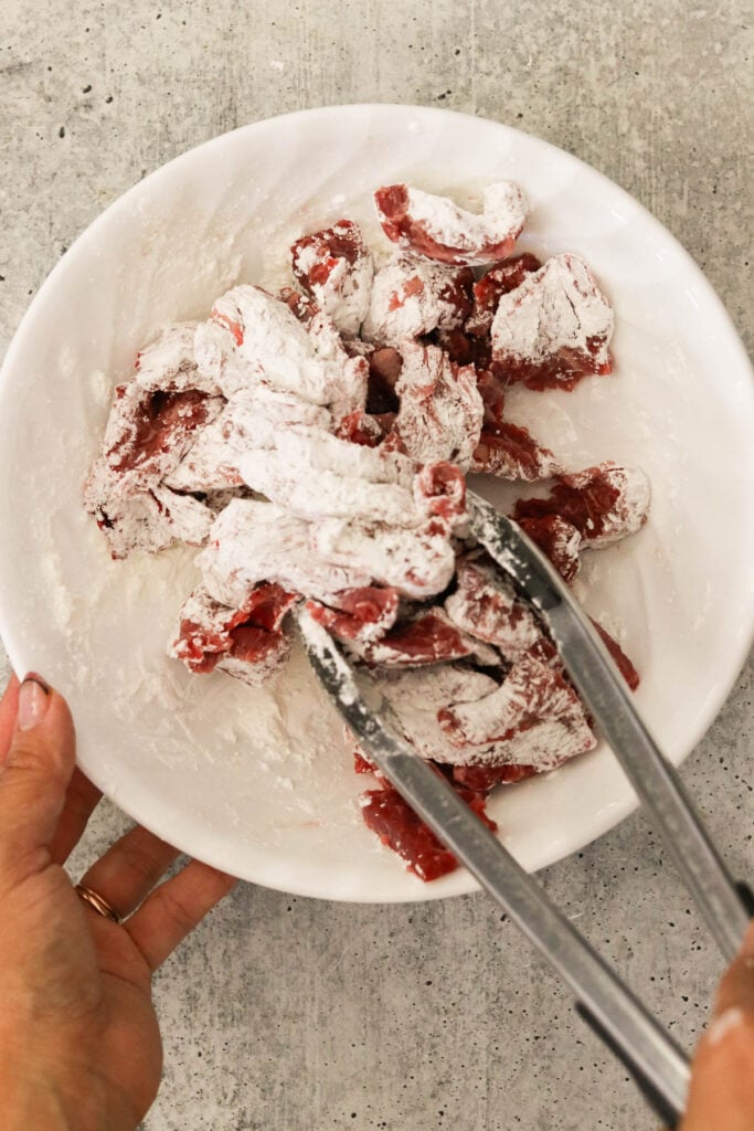 Flank steak slices coated in cornstarch in a mixing bowl