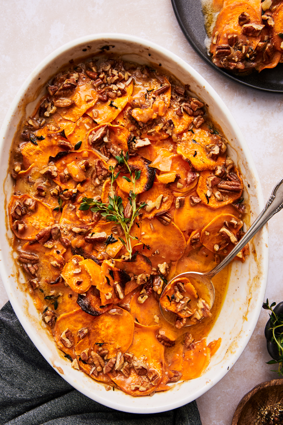 scalloped sweet potatoes in a baking dish with a spoon resting inside