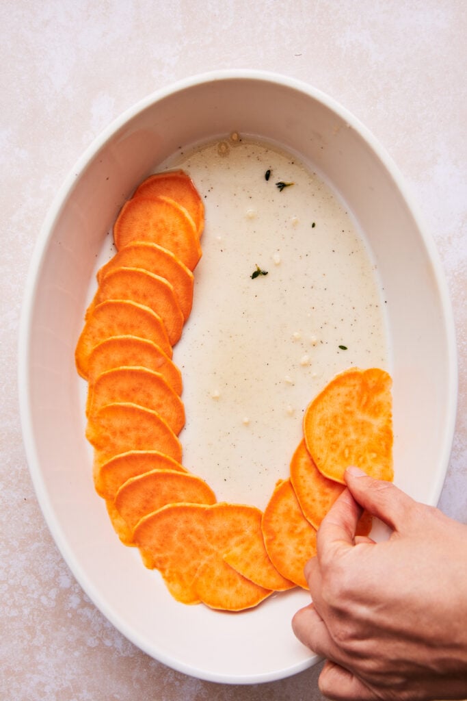 placing sliced sweet potatoes in a baking dish