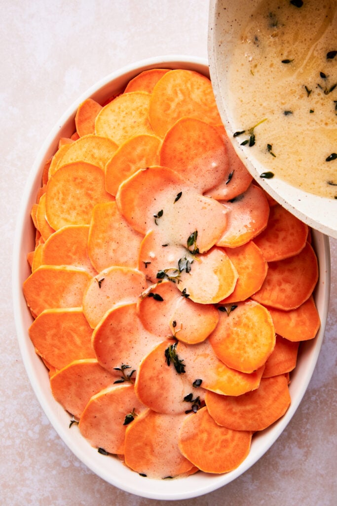 pouring sauce over the top of the sliced potatoes