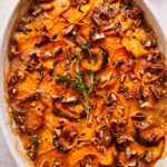 scalloped sweet potatoes in a baking dish topped with fresh herbs