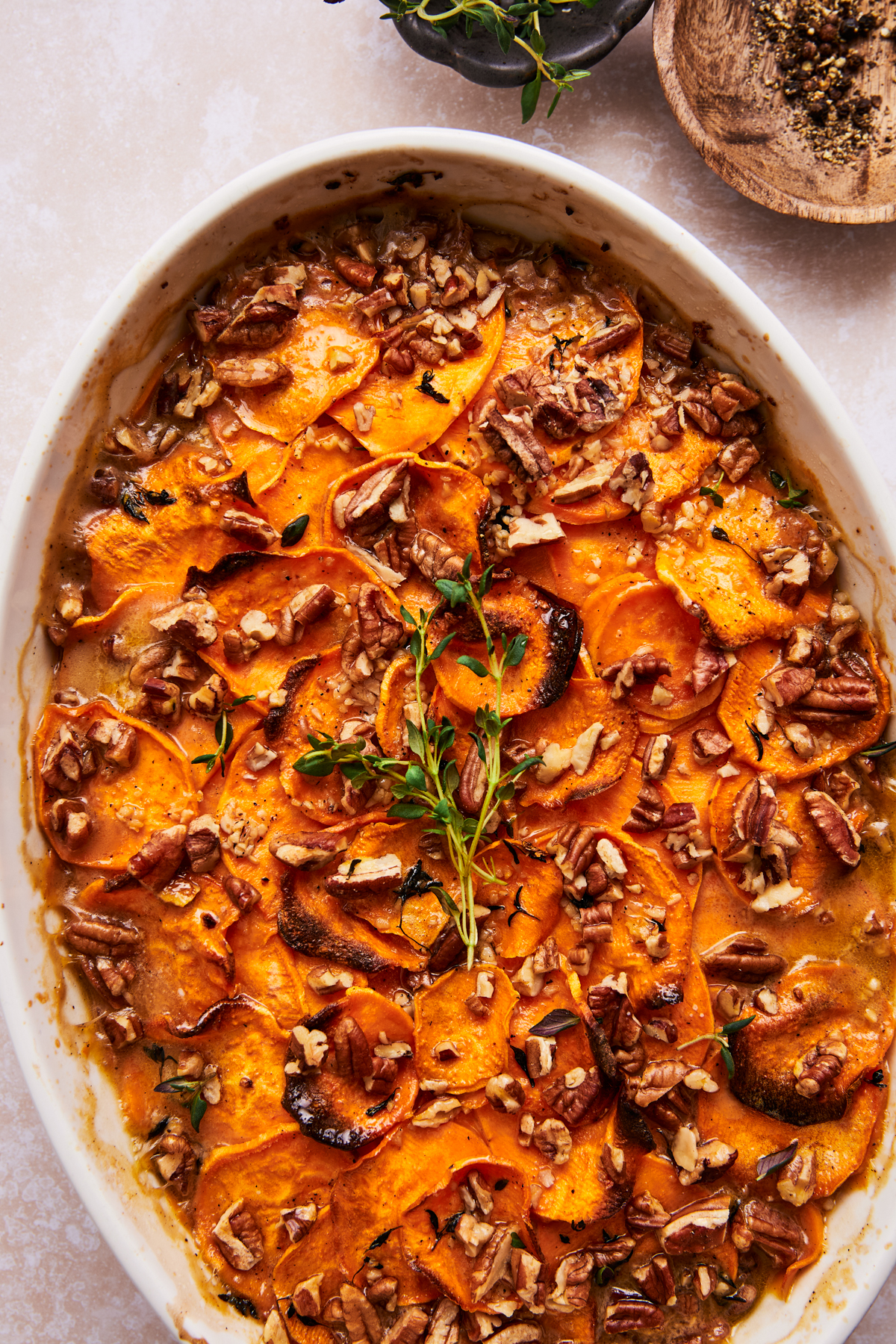 scalloped sweet potatoes in a baking dish topped with fresh herbs