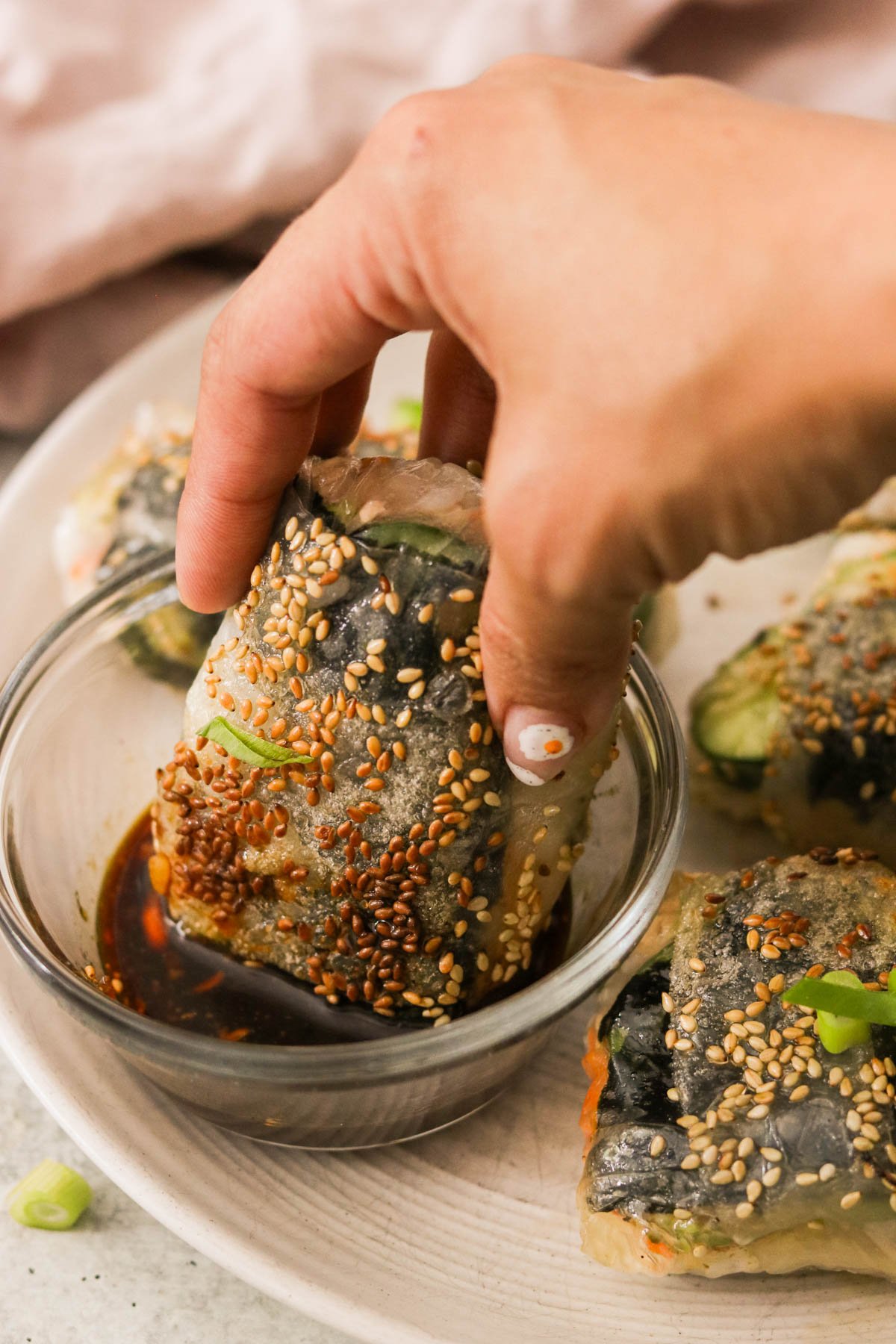 dipping a rice paper sushi roll into a small bowl of dipping sauce