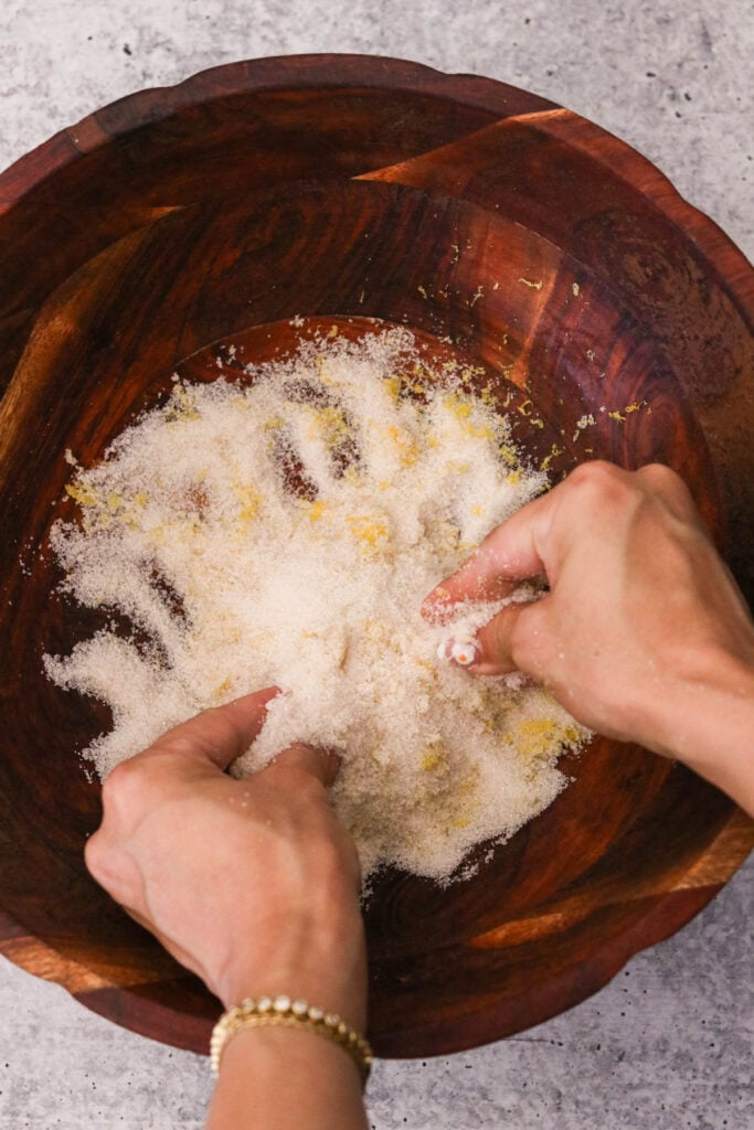 Zest being rubbed into sugar by hand in a glass bowl