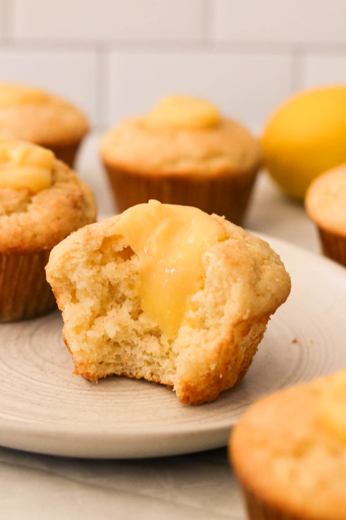Bright and fluffy gluten-free lemon curd muffins on a plate, one cut open to show creamy lemon curd center

