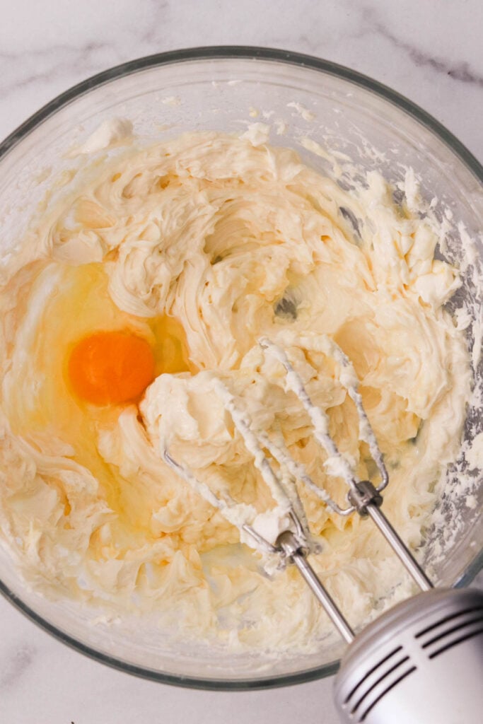 adding an egg one at a time to the cheesecake filling
