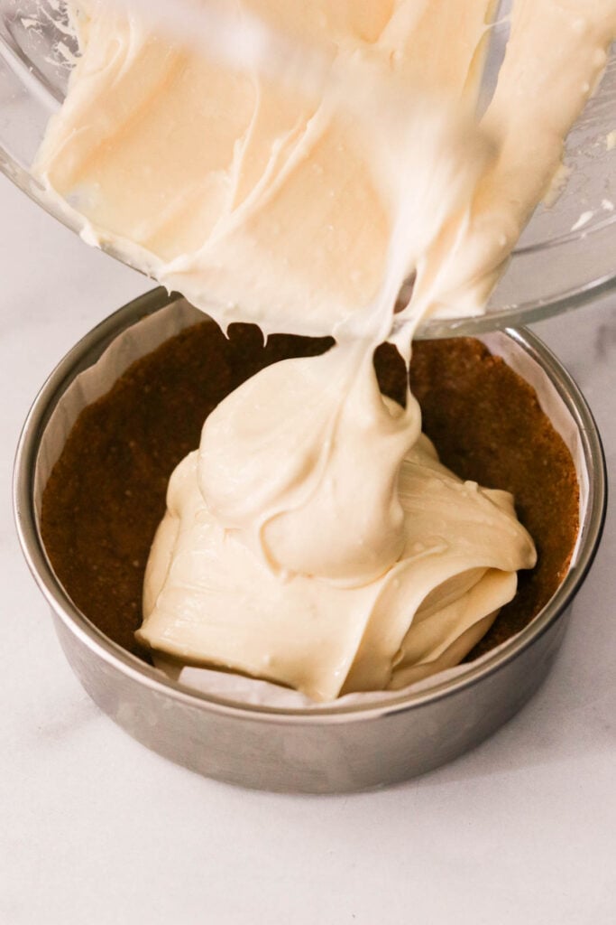 placing the cheesecake filling onto the pan with the crust
