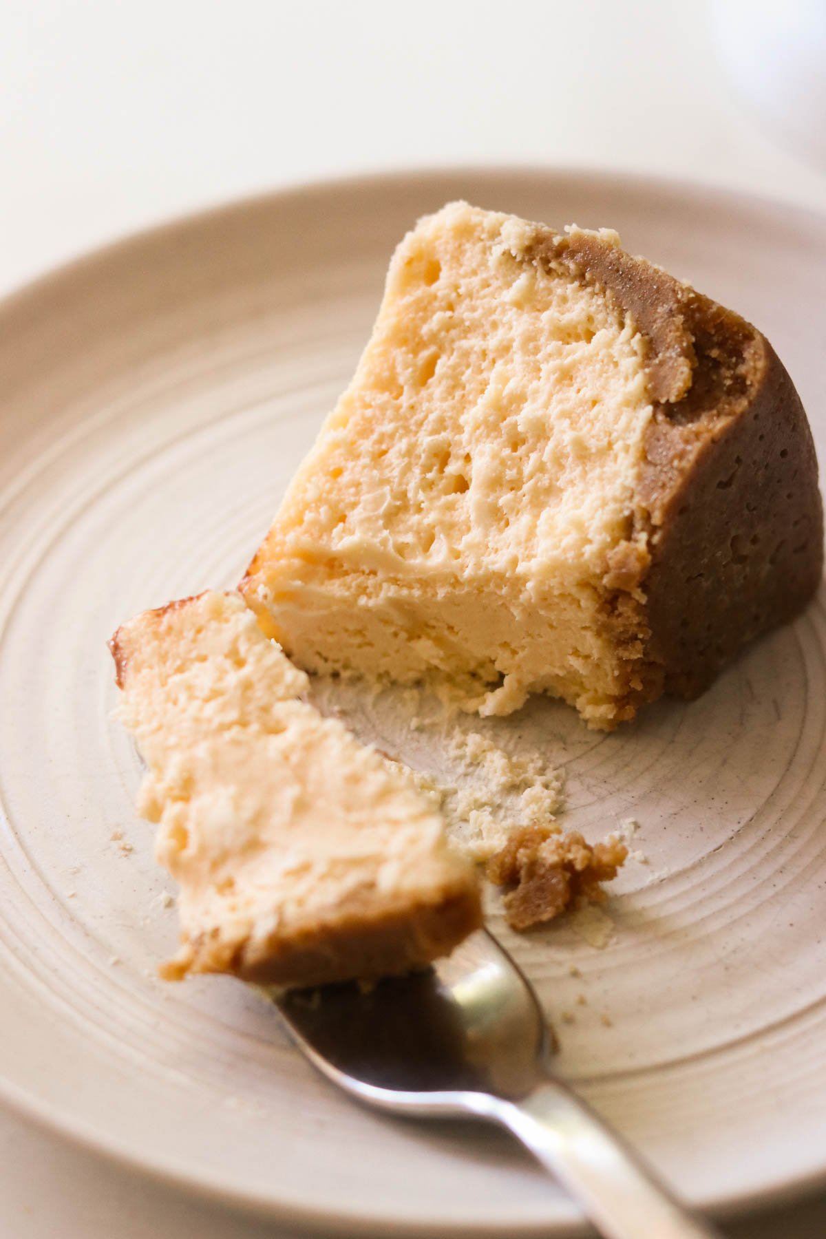 a slice of cheesecake on a white plate with a fork lifting a bite off.