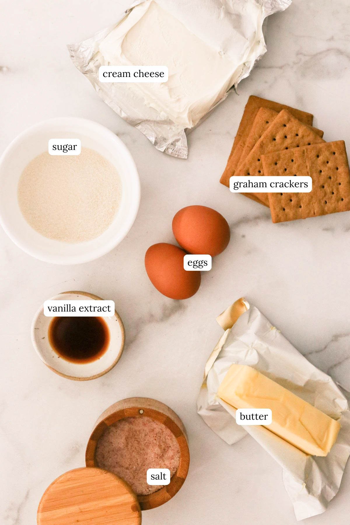 a flat lay of ingredients on a marble countertop for a simple cheesecake with a graham cracker crust.