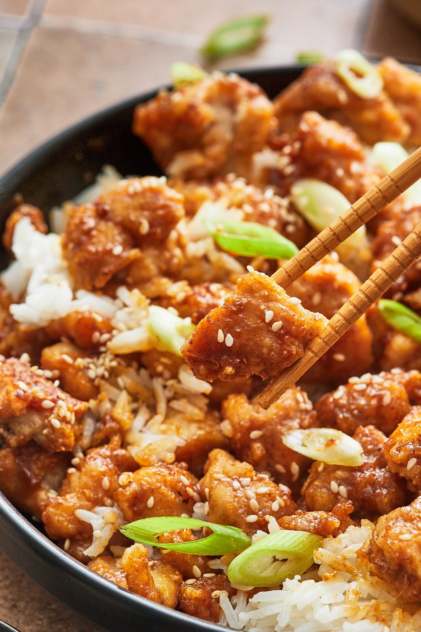 chopsticks picking up a piece of crispy sesame chicken 