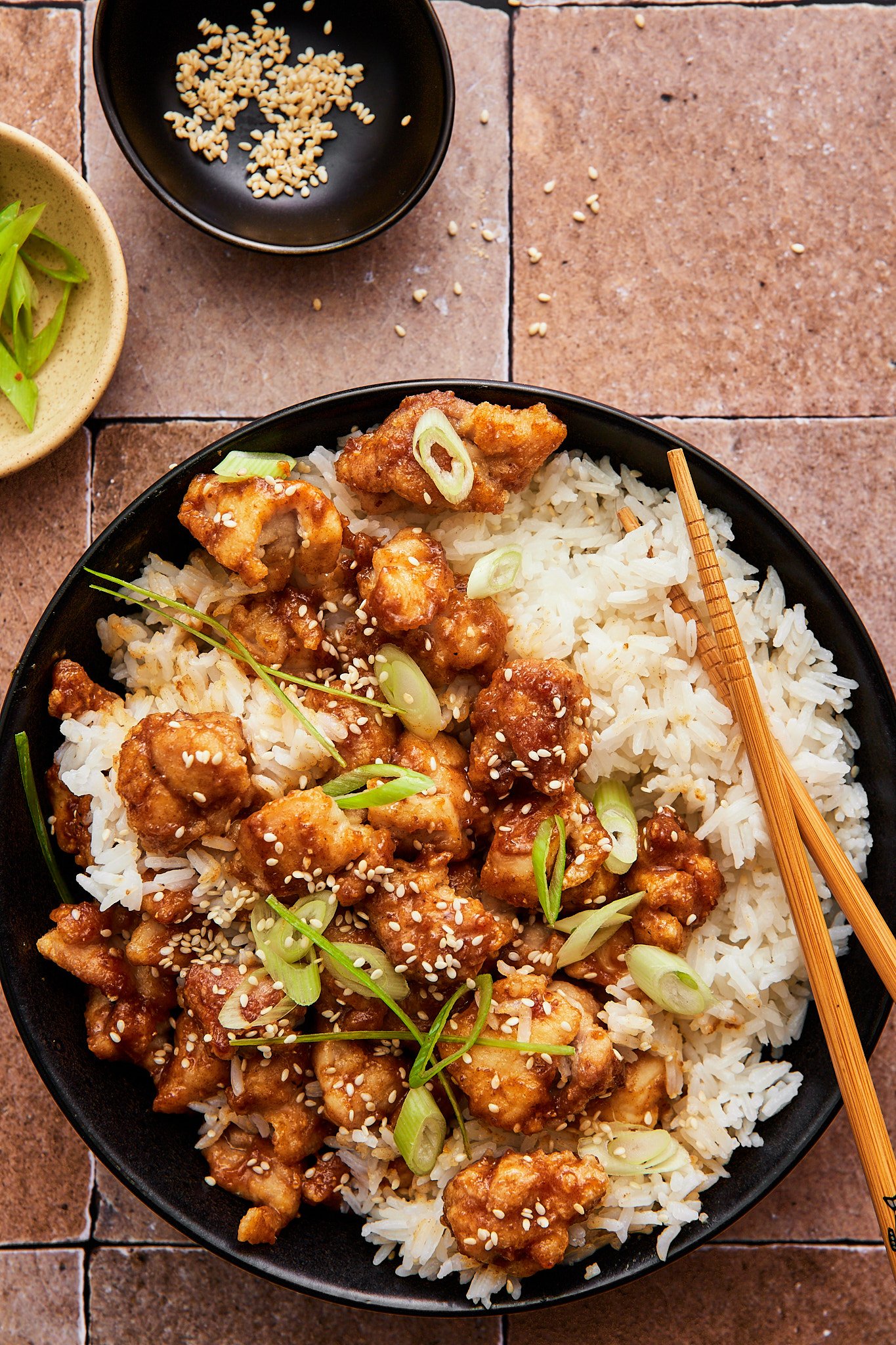 air fryer sesame chicken atop a bowl of fluffy white rice topped with scallions and sesame seeds 