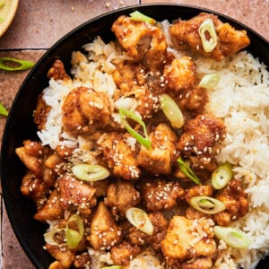 crispy air fryer sesame chicken atop a bed of white rice topped with green onions