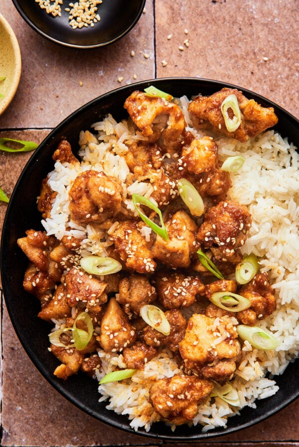crispy air fryer sesame chicken atop a bed of white rice topped with green onions