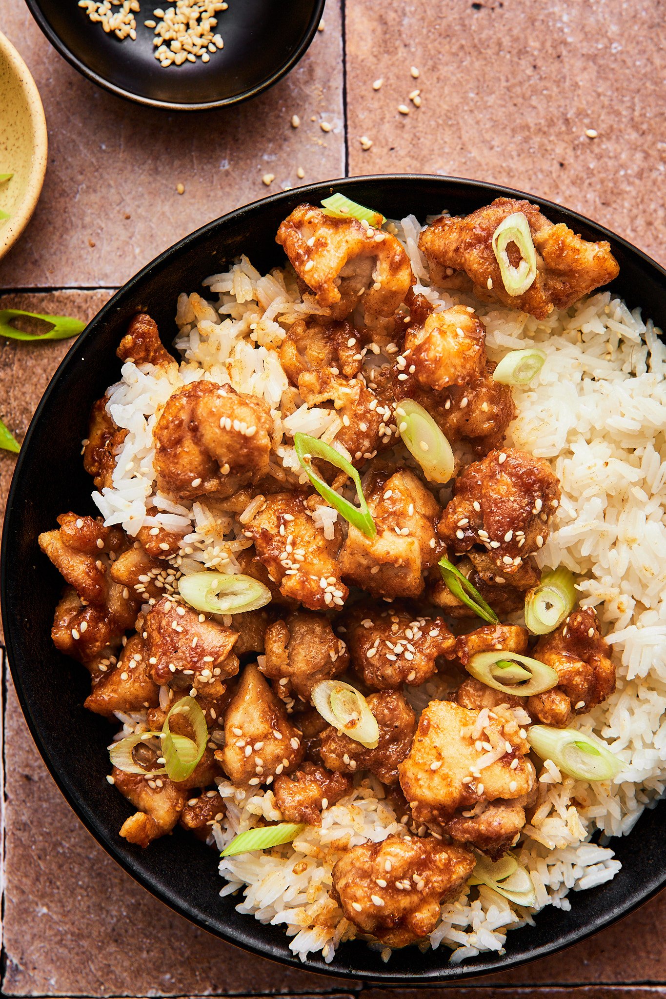 crispy air fryer sesame chicken atop a bed of white rice topped with green onions