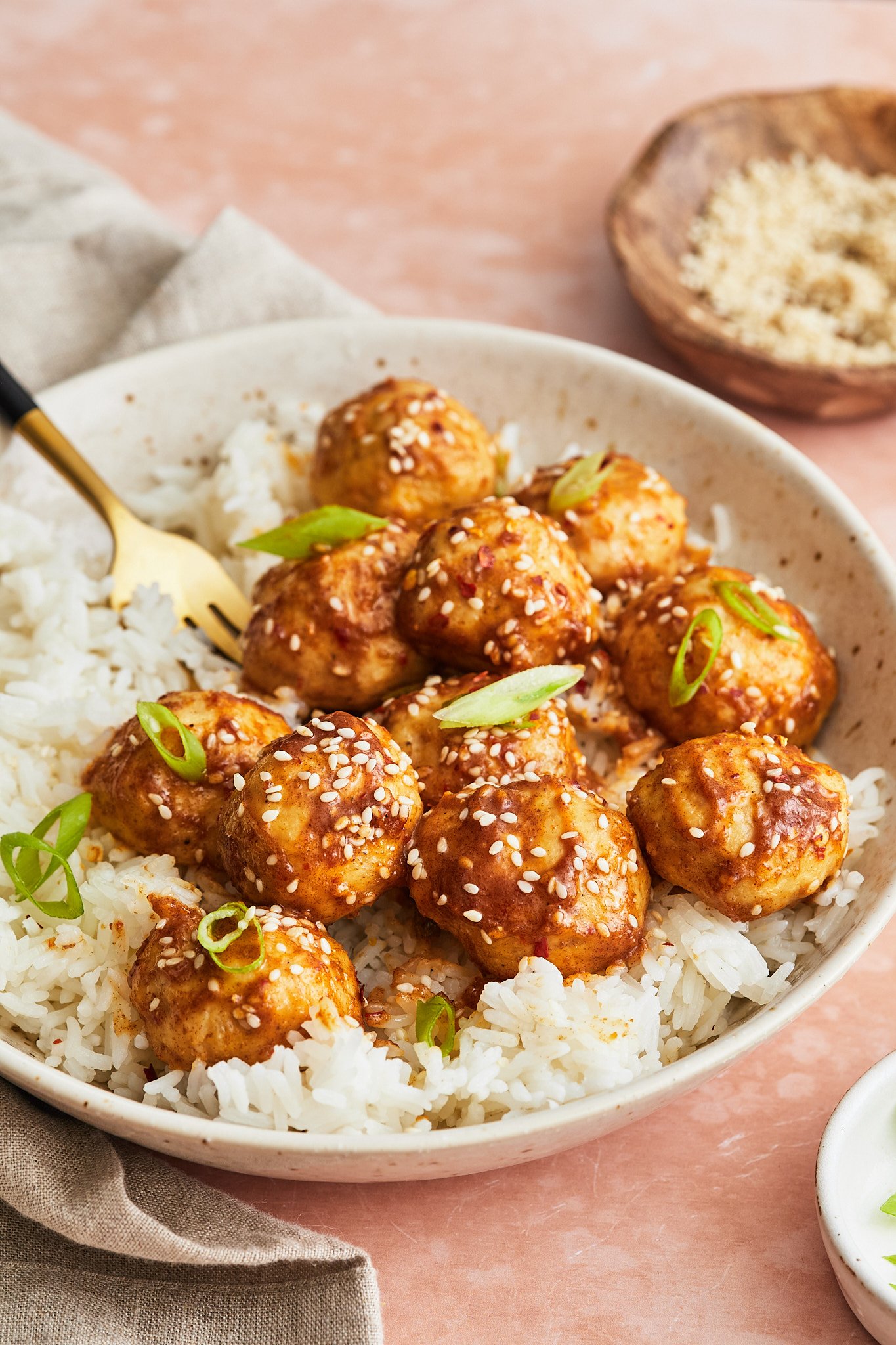 sticky asian meatballs atop a bed of rice and topped with scallions and sesame seeds