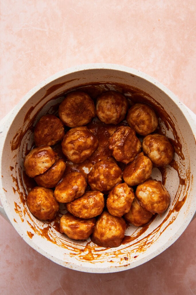 adding the cooked meatballs to the sauce in a saucepan