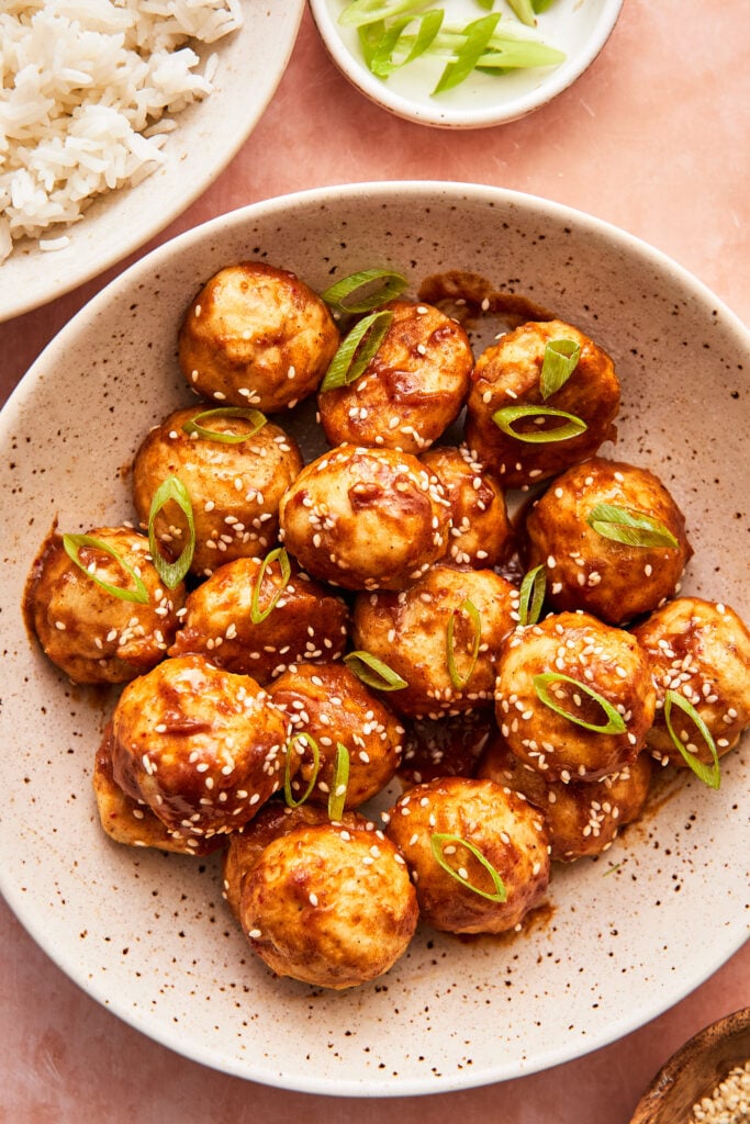 sticky asian meatballs served in a large bowl topped with scallions and sesame seeds 