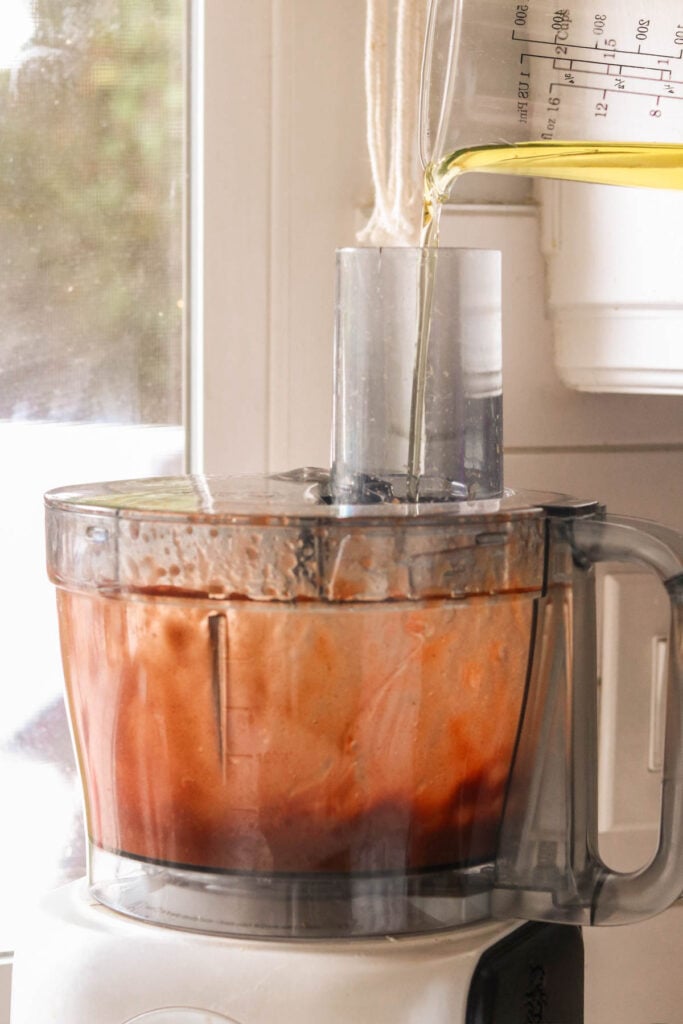 Food processor bowl with ingredients for Catalina dressing—vinegar, ketchup, spices—being blended into a smooth vinaigrette
