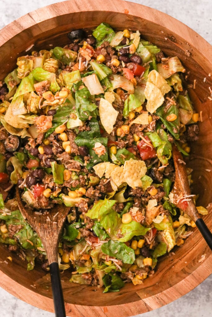 Close-up of tossing the assembled taco salad with Catalina dressing coating every ingredient