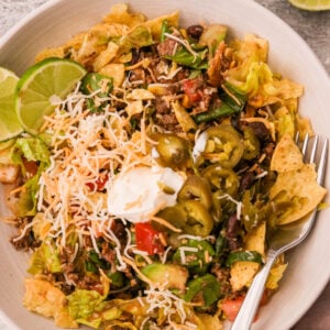 Overhead shot of a vibrant taco salad bowl with seasoned beef, beans, corn, avocado, olives, cheese, and crushed tortilla chips, drizzled in Catalina dressing