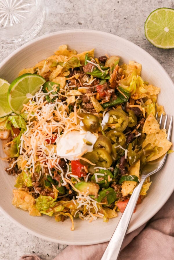 Overhead shot of a vibrant taco salad bowl with seasoned beef, beans, corn, avocado, olives, cheese, and crushed tortilla chips, drizzled in Catalina dressing