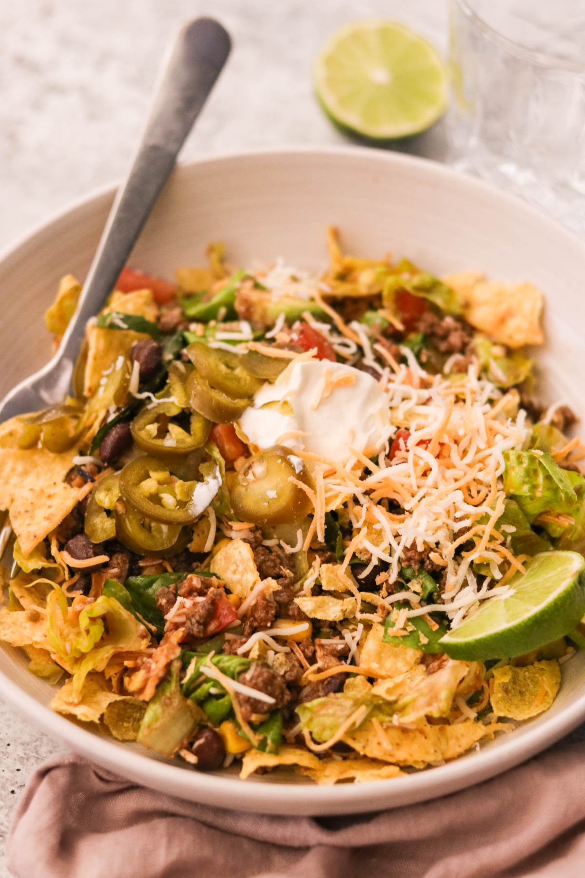Overhead shot of a vibrant taco salad bowl with seasoned beef, beans, corn, avocado, olives, cheese, and crushed tortilla chips, drizzled in Catalina dressing