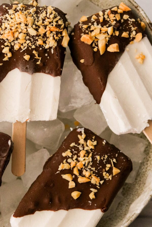 coconut ice cream bars coated in chocolate and chopped nuts in a bowl filled with ice cubes