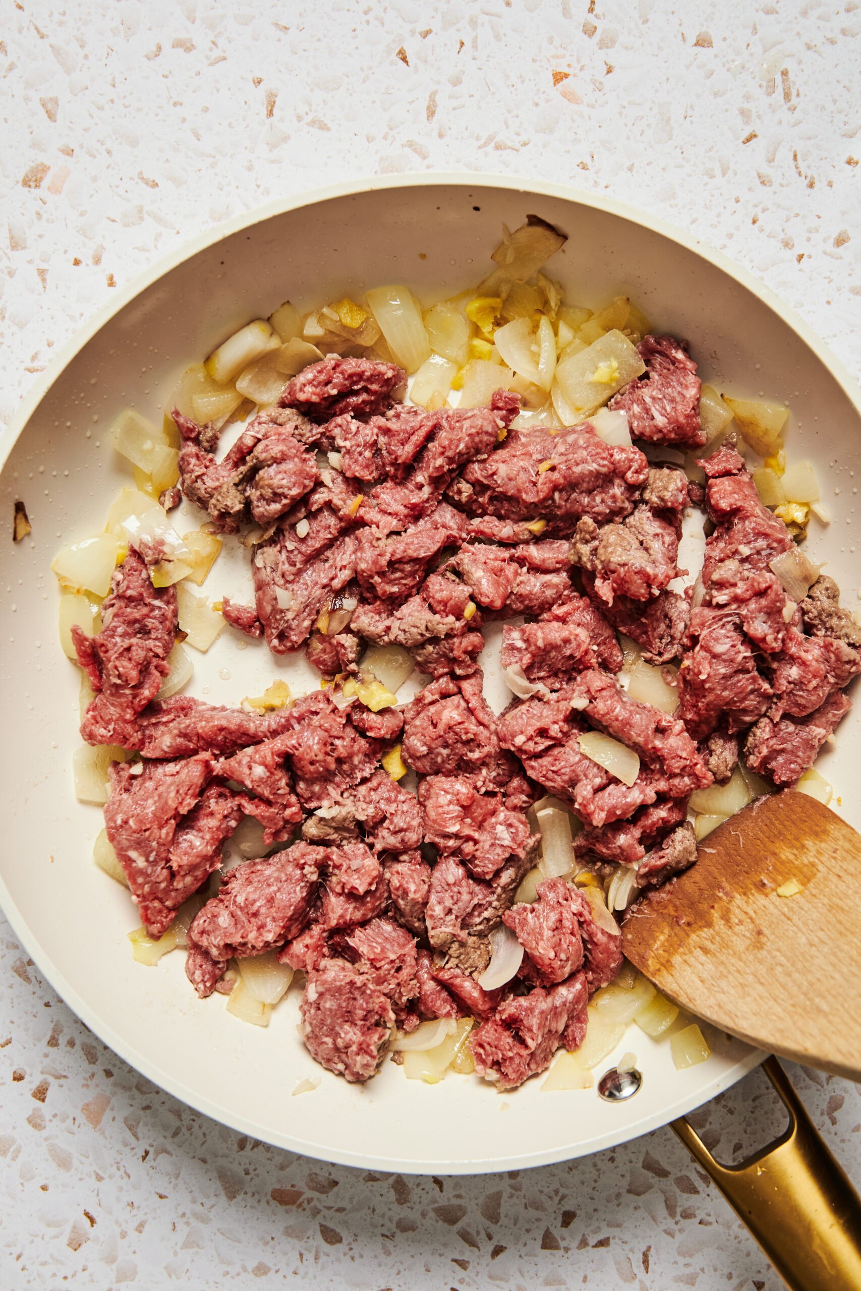 Raw ground beef in a pan with sautéed onion, garlic, and ginger.