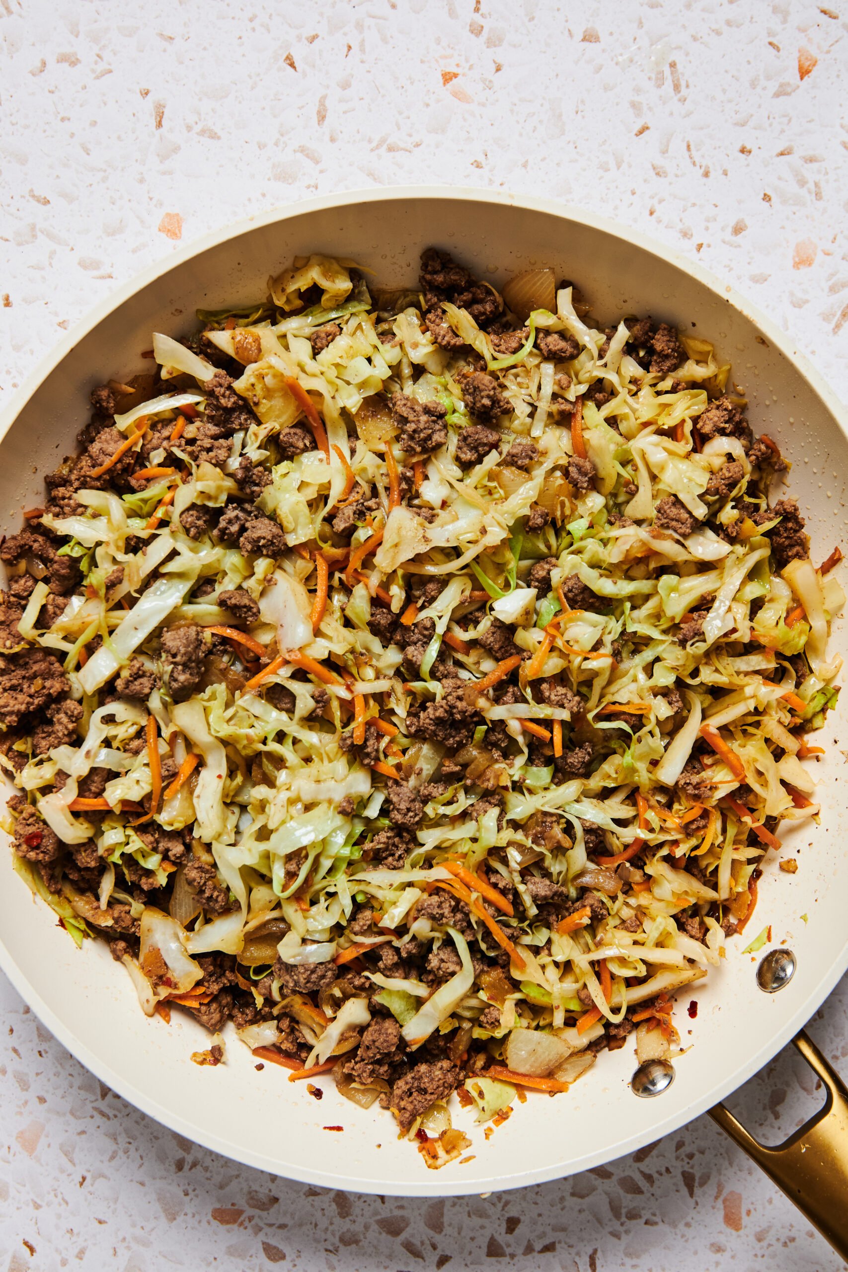 Asian ground beef and cabbage stir fry in a large pan on a speckled white countertop.