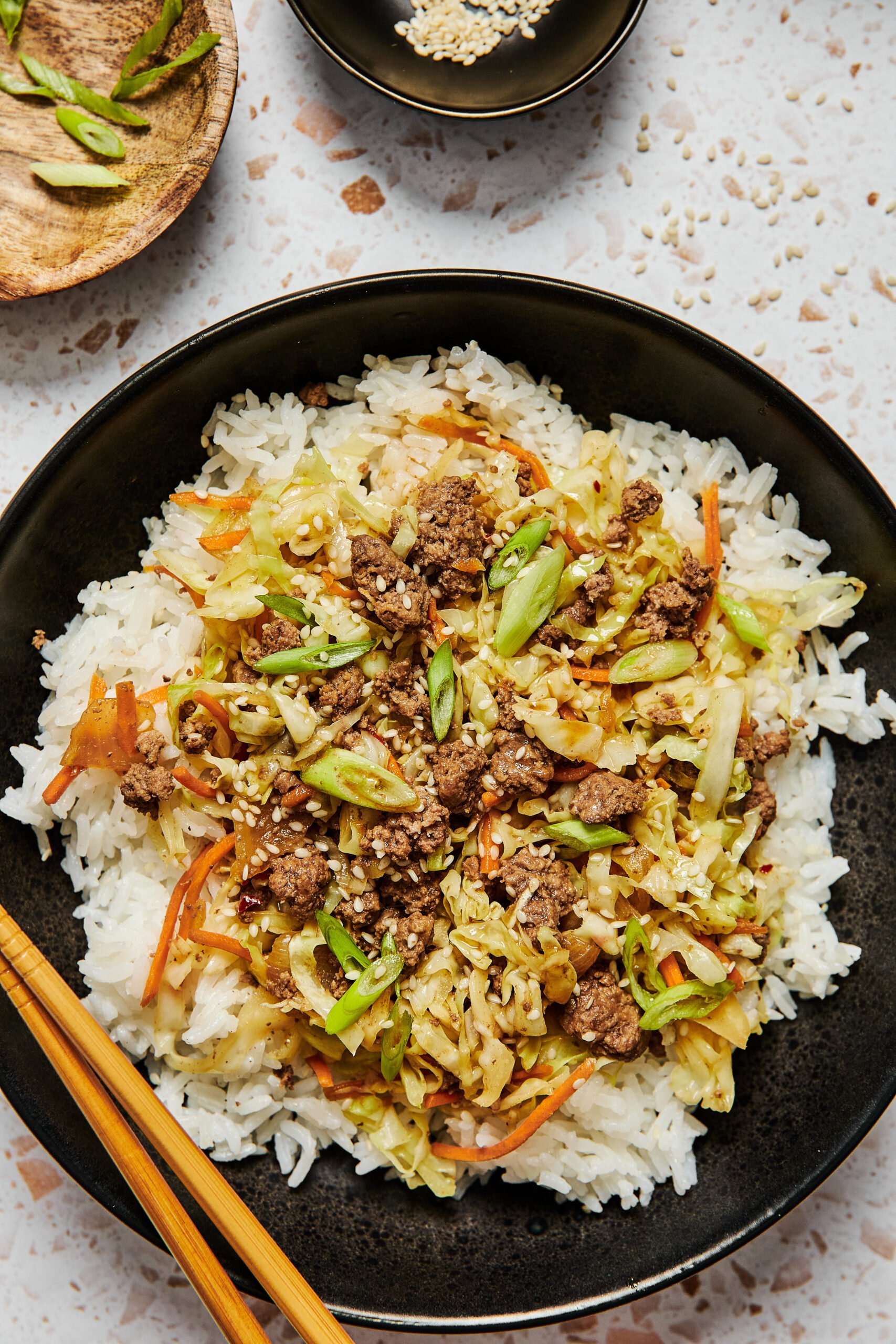 Asian ground beef and cabbage stir fry served over white rice in a black bowl with chopsticks on the side.