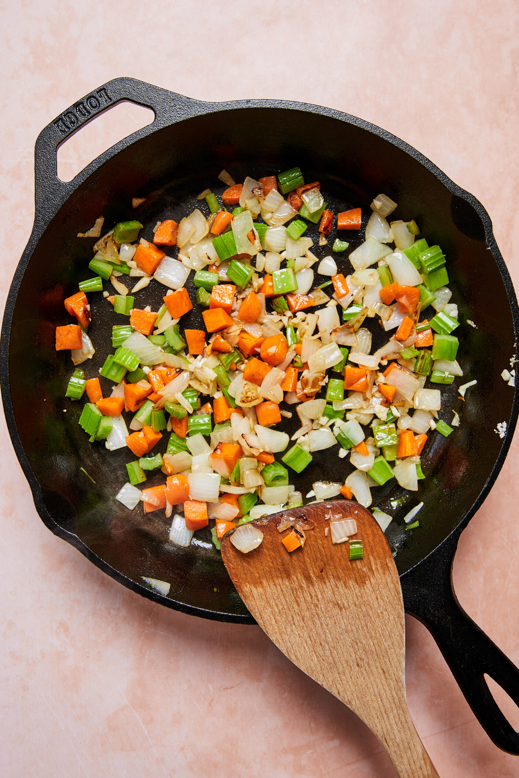 Onion, celery, and carrot sautéing in a black oven-safe skillet with ghee.