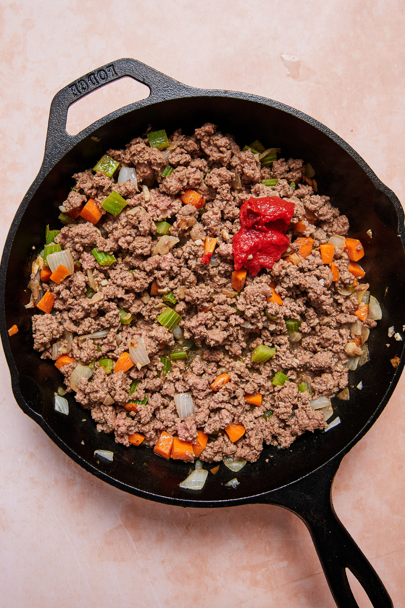 Ground beef browning in a black oven-safe skillet with vegetables and tomato paste.