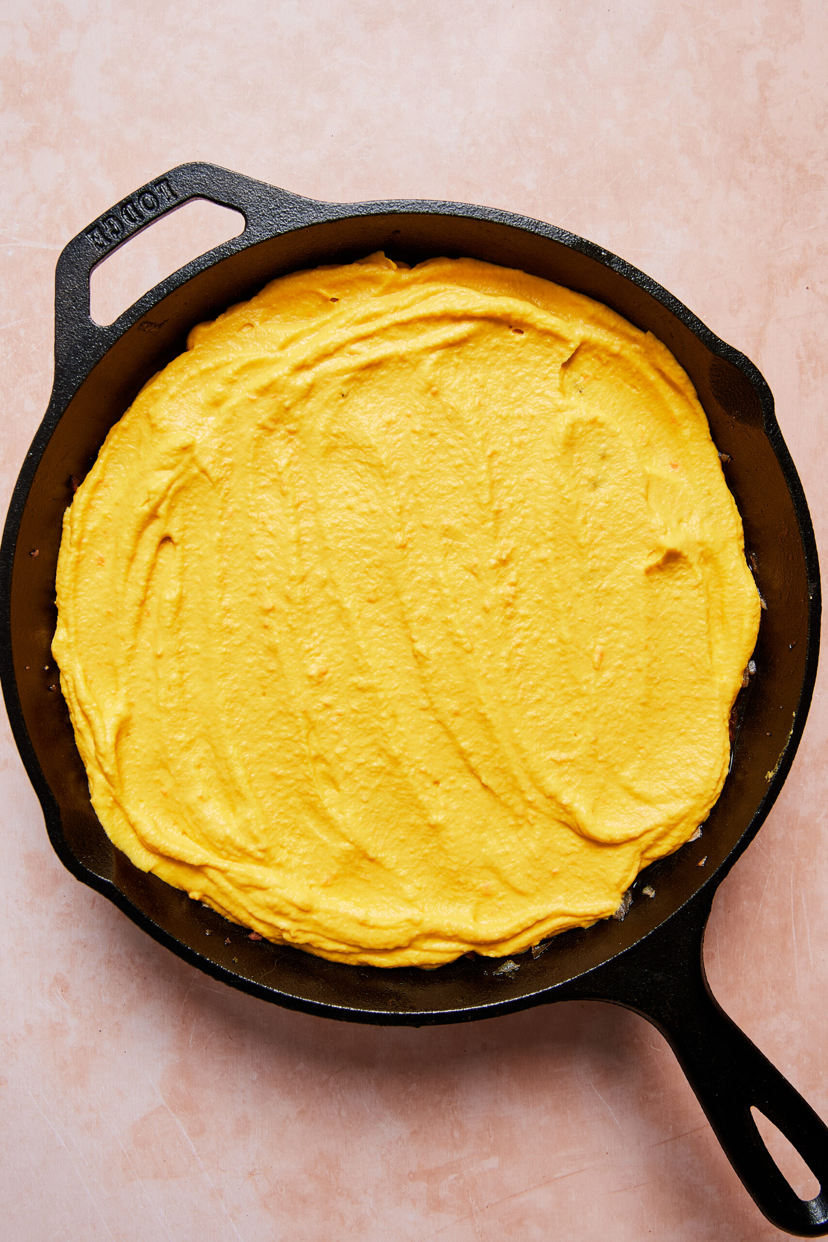 Cauliflower and carrot mash spread evenly over the meat filling in a black oven-safe skillet before baking.