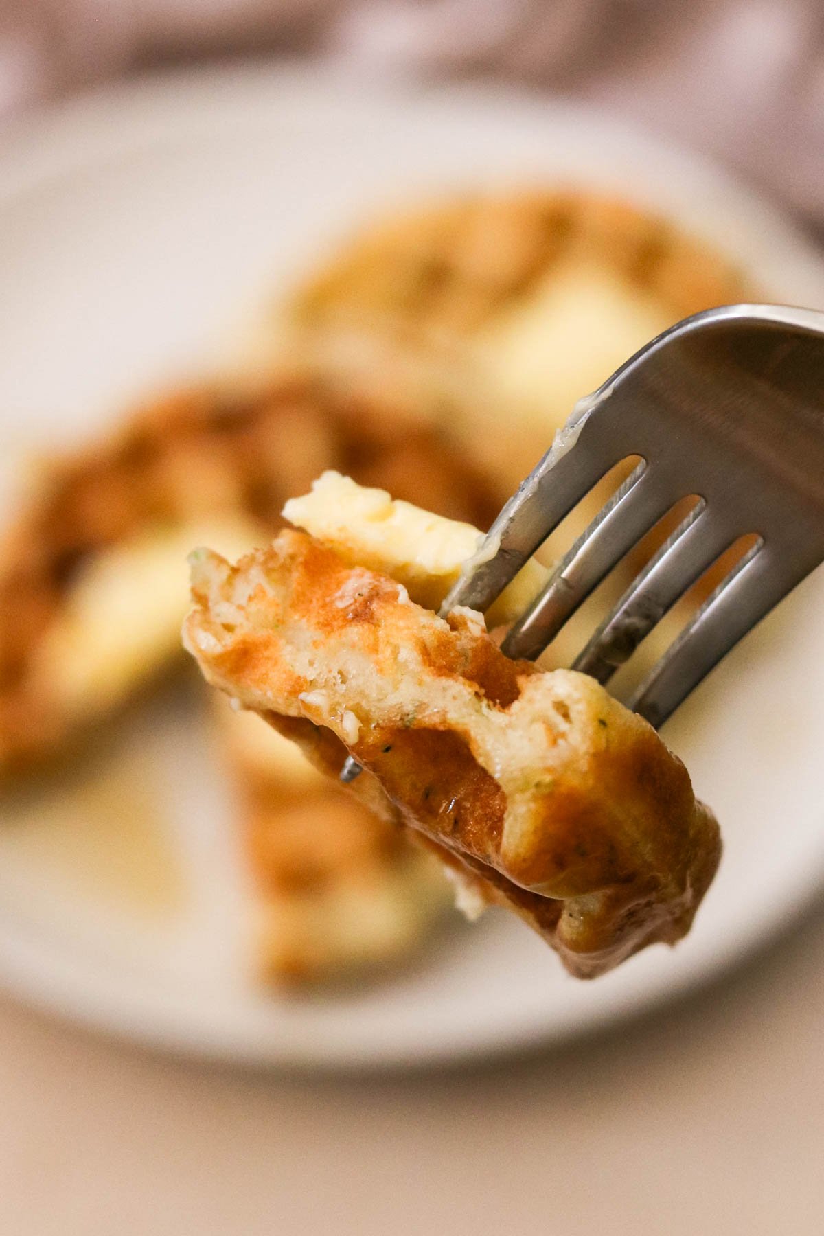 a fork holding a bite of waffles topped with butter and maple syrup