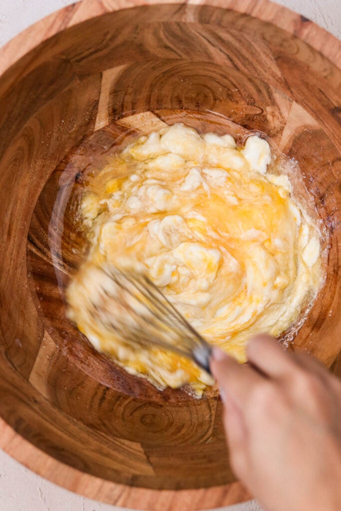 Ricotta, egg, oil, sugar, and vanilla being whisked together in a wooden bowl